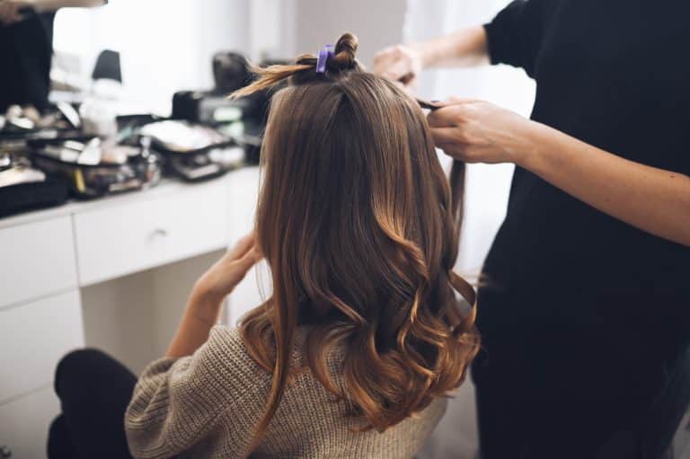 Hair stylist prepares woman makes curls hairstyle with curling iron. Long light brown natural hair