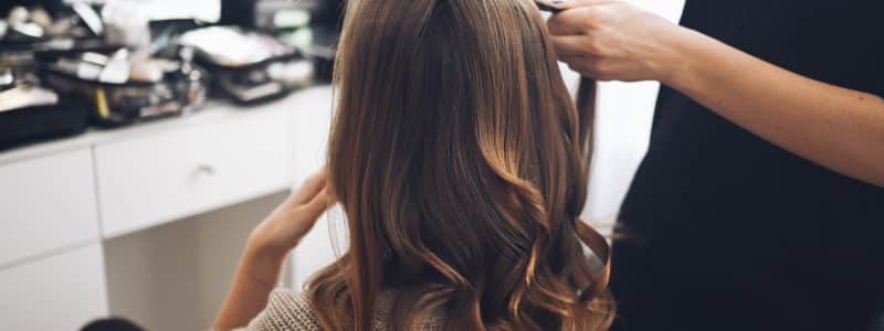 Hair stylist prepares woman makes curls hairstyle with curling iron. Long light brown natural hair
