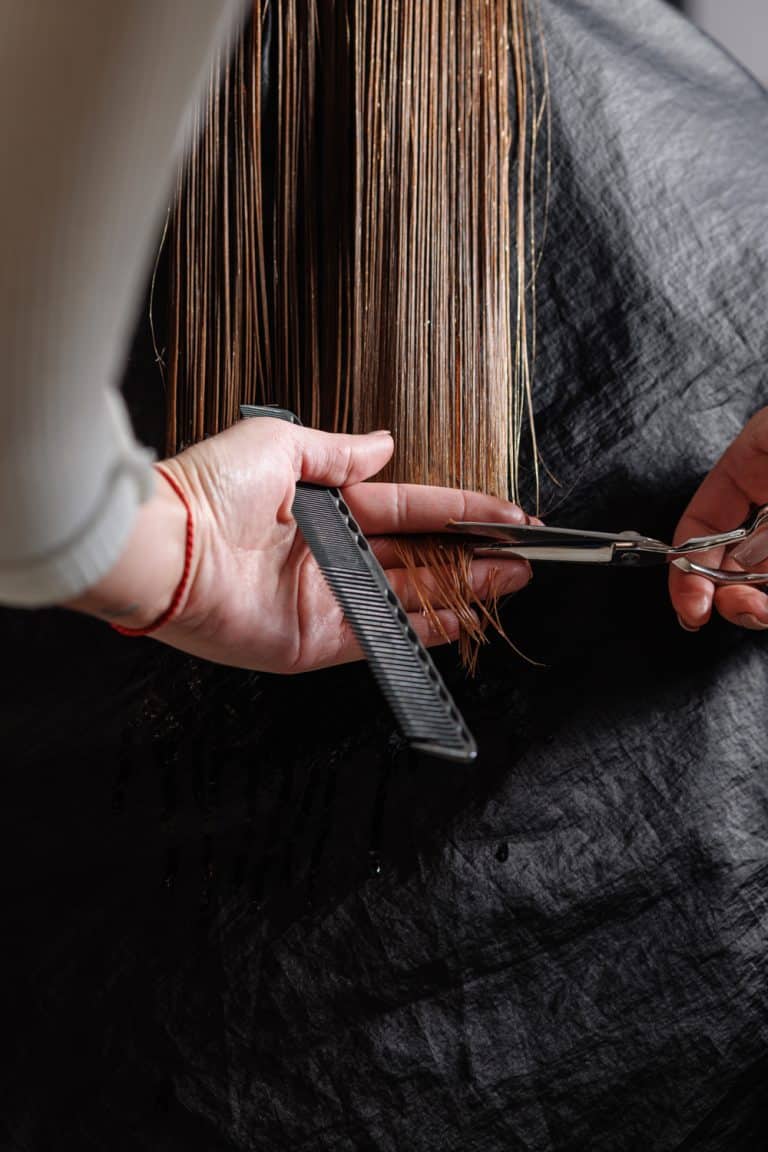 hairdresser makes a haircut to a woman in the salon. The hairdresser cuts wet hair, combing with a comb. client with short hair. back view