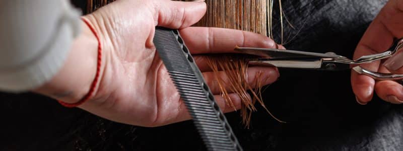 hairdresser makes a haircut to a woman in the salon. The hairdresser cuts wet hair, combing with a comb. client with short hair. back view