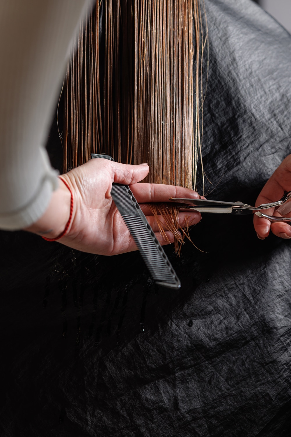 hairdresser makes a haircut to a woman in the salon. The hairdresser cuts wet hair, combing with a comb. client with short hair. back view